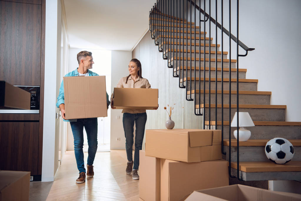 casal feliz andando com caixas e sorrindo em nova casa
  - Foto, Imagem