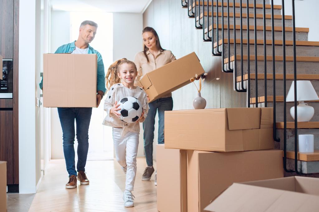 cheerful kid holding football with happy parents with boxes on background  - Photo, Image