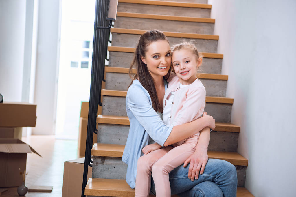 alegre mujer sentado con hija en escaleras en nuevo hogar
  - Foto, imagen