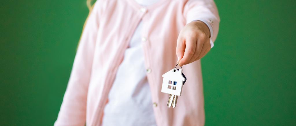 abgeschnittene Ansicht von Kind hält Haus geformten Schlüsselanhänger isoliert auf grün - Foto, Bild