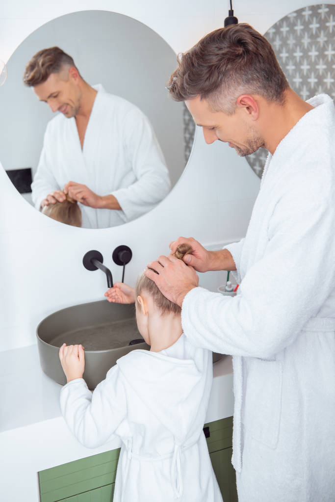 pai carinhoso fazendo o cabelo da filha de pé no banheiro
  - Foto, Imagem