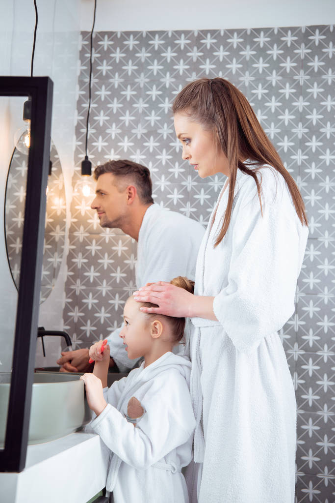 man die in de buurt van vrouw met dochter bedrijf tandenborstel in de badkamer - Foto, afbeelding