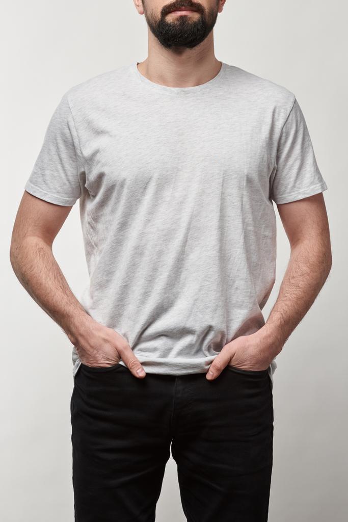 обрезанный вид бородатого человека с руками в карманах в белой футболке с копировальным пространством, изолированным на сером
 - Фото, изображение