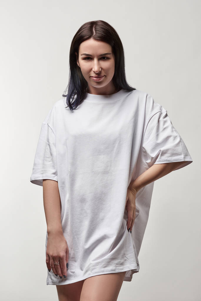 hermosa mujer joven en blanco camiseta de gran tamaño con espacio de copia mirando a la cámara aislada en gris
 - Foto, Imagen