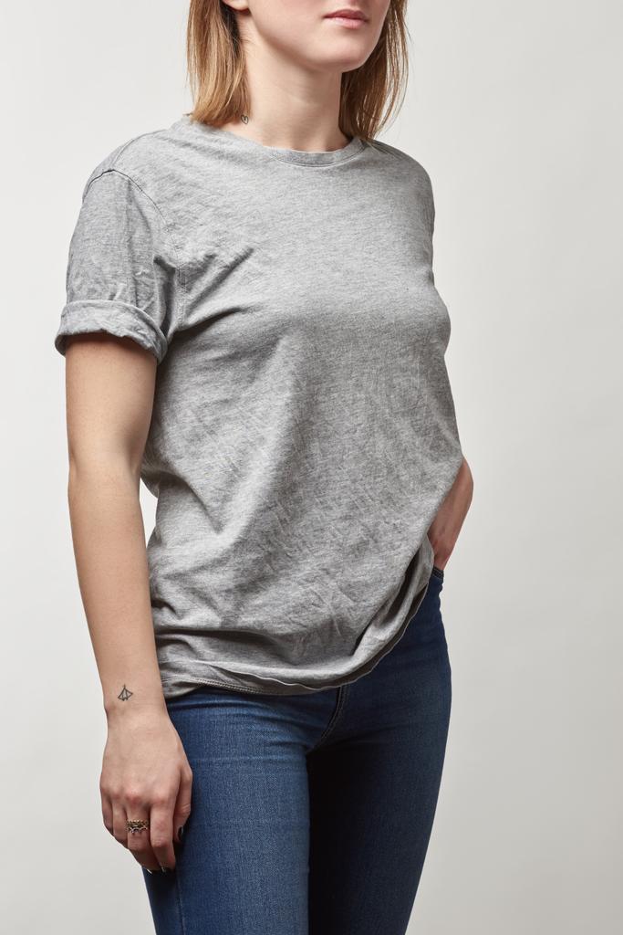 обрезанный вид молодой женщины в джинсах и серой футболке с копировальным пространством, изолированным на белом
 - Фото, изображение