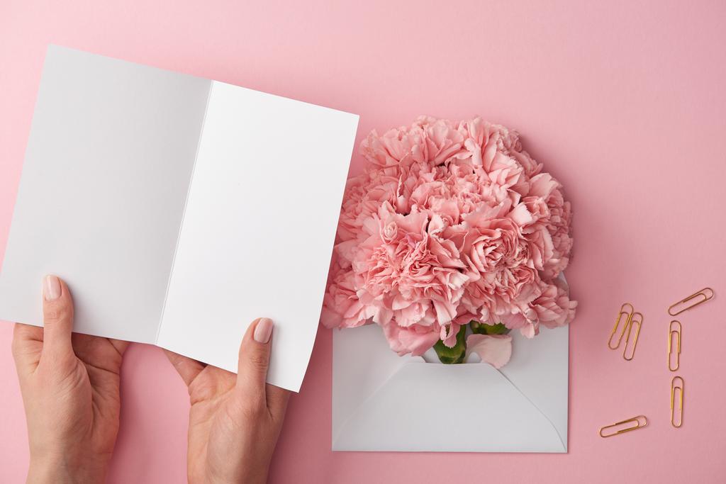 ピンクに分離された封筒で空白のカードとピンクの花を持つ女性のクロップ撮影 - 写真・画像