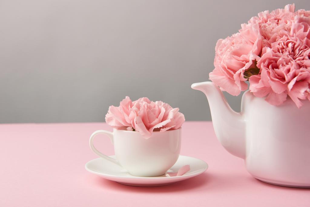 vergrote weergave van de prachtige tere roze bloemen in witte theepot en kopje op grijs    - Foto, afbeelding