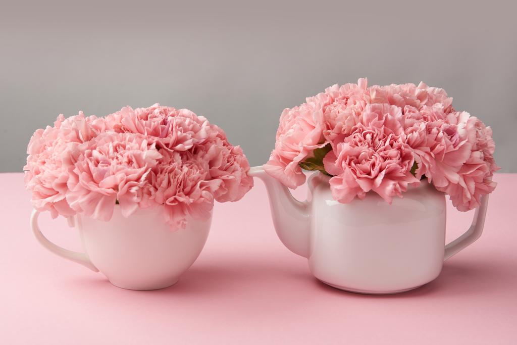 beautiful tender pink flowers in white teapot and cup on grey  - Photo, Image