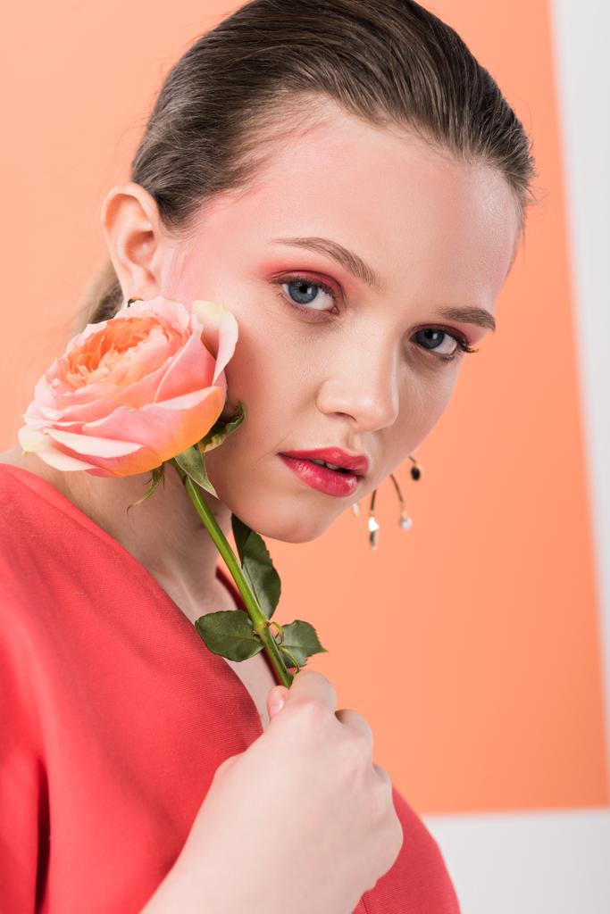 beautiful stylish girl holding rose, looking at camera and posing with living coral on background - Photo, Image