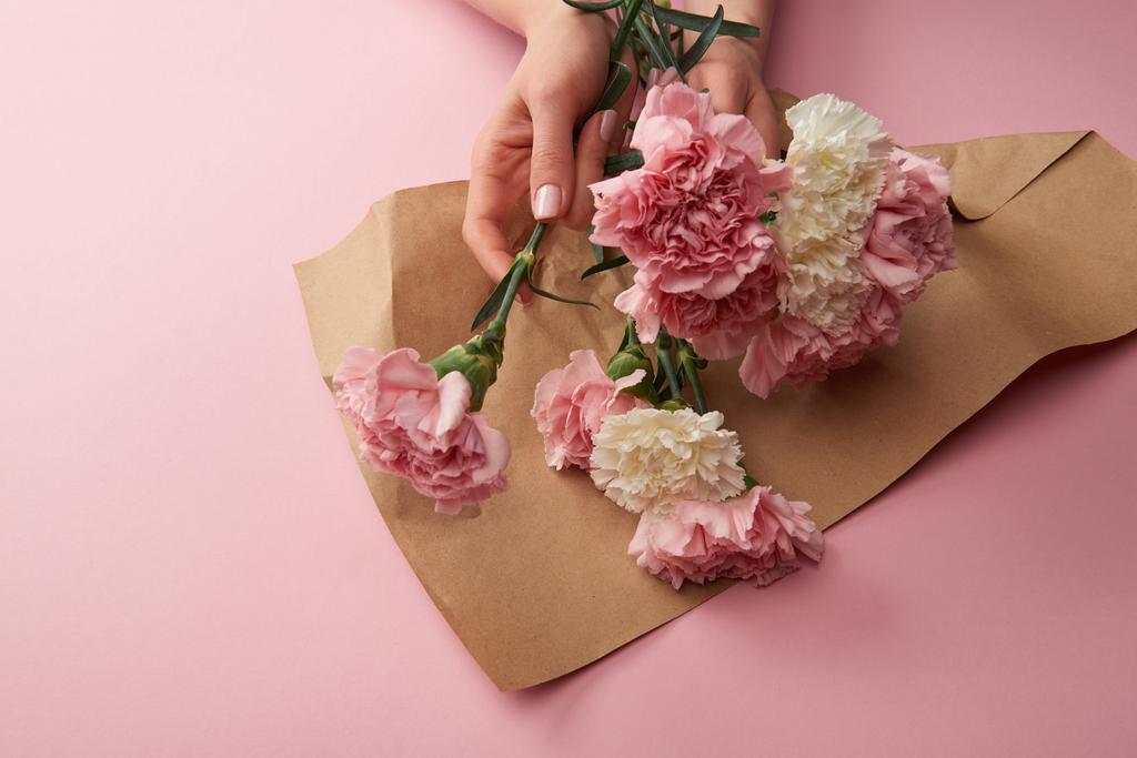 abgeschnittene Aufnahme einer Frau, die schöne Blumen in Bastelpapier auf rosa einwickelt - Foto, Bild