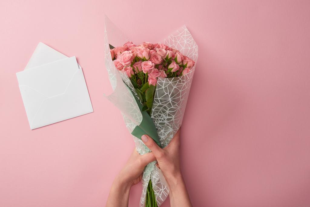 bijgesneden schot van vrouw met mooie rozen en witte envelop geïsoleerd op roze boeket - Foto, afbeelding
