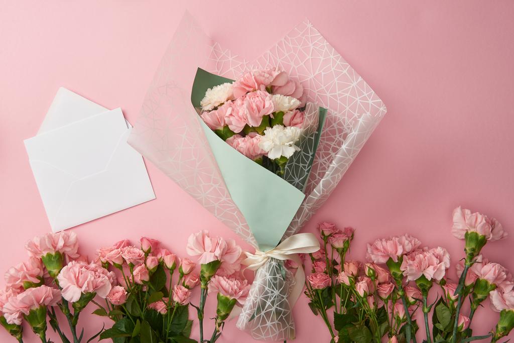 bovenaanzicht van prachtige boeket, tere roze bloemen en witte envelop met kaart geïsoleerd op roze - Foto, afbeelding