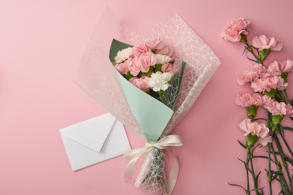 όμορφη ανθοδέσμη, ροζ γαρύφαλλο λουλούδια και λευκό φάκελο που απομονώνονται σε ροζ  - Φωτογραφία, εικόνα