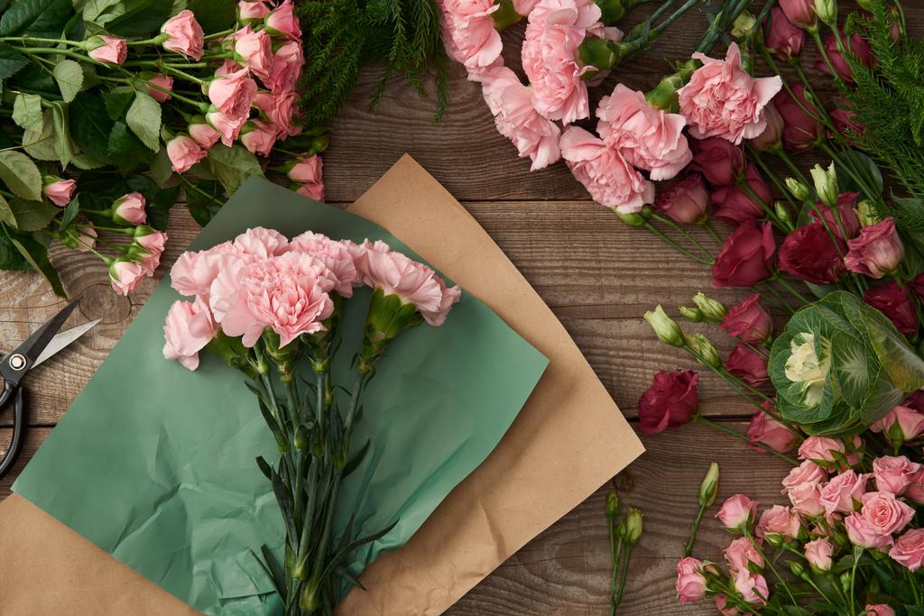 κάτοψη της όμορφης, διάφορα λουλούδια, χαρτί Κραφτ και ψαλιδιού σε ξύλινη επιφάνεια  - Φωτογραφία, εικόνα