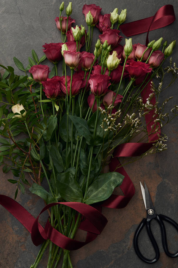 vue de dessus de belles fleurs d'eustomes rouges avec ruban et ciseaux sur une surface sombre
    - Photo, image