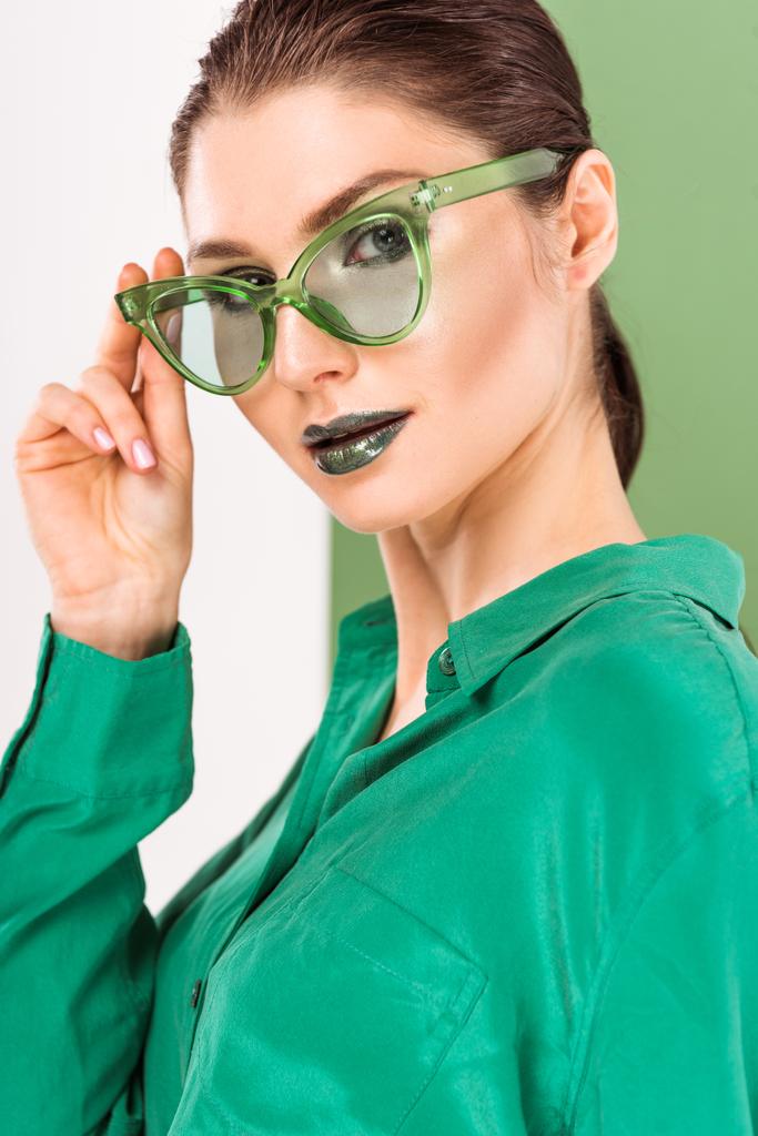 beautiful fashionable woman in sunglasses posing and looking at camera with sea green on background - Photo, Image