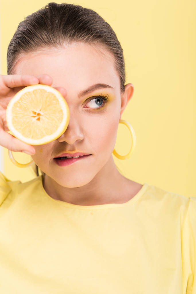 hermosa chica elegante sosteniendo limón, mordiendo el labio y posando aislado en el centro de atención
 - Foto, Imagen