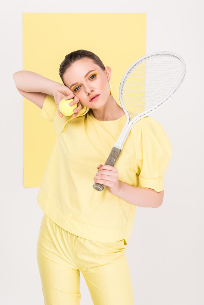 hermosa chica con estilo con raqueta de tenis y bola mirando a la cámara mientras posando con centro de atención en el fondo
 - Foto, imagen
