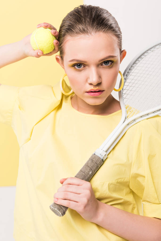 kaunis tyylikäs tyttö tennismaila ja pallo katselee kameraa poseeratessaan parrasvaloissa taustalla
 - Valokuva, kuva