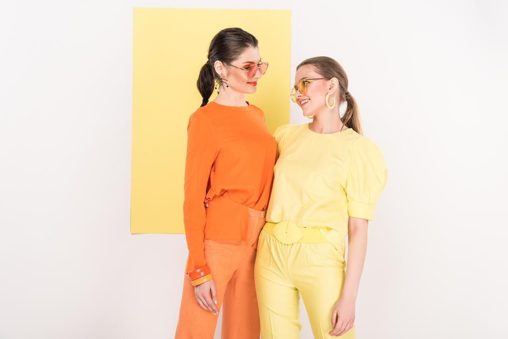 mooie lachende stijlvolle meisjes in zonnebril poseren met schijnwerpers op achtergrond - Foto, afbeelding