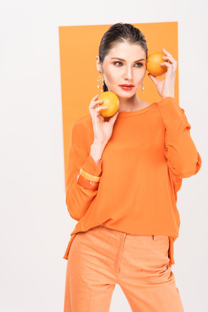 beautiful stylish woman holding oranges, looking away and posing with turmeric on background - Photo, Image