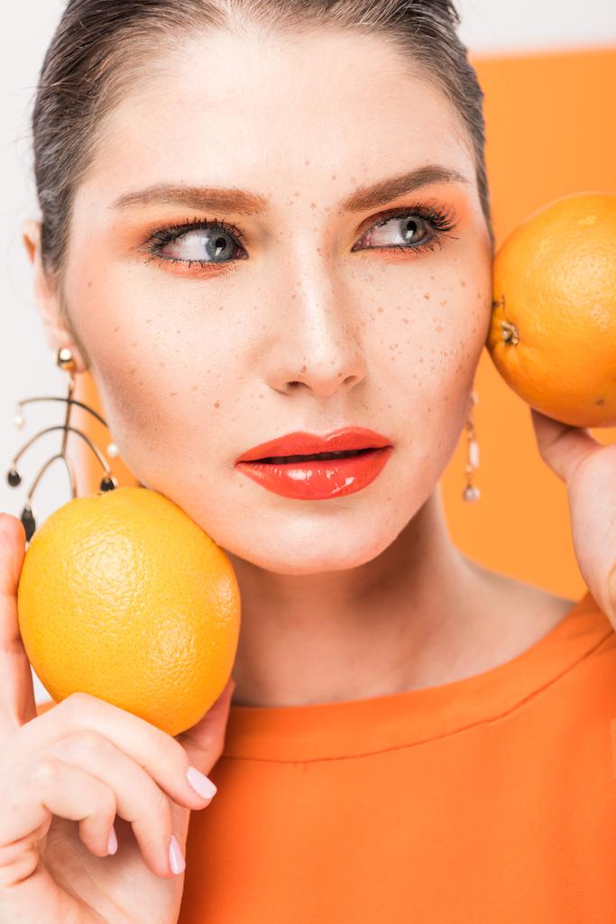 beautiful stylish woman holding oranges, looking away and posing with turmeric on background - Photo, Image