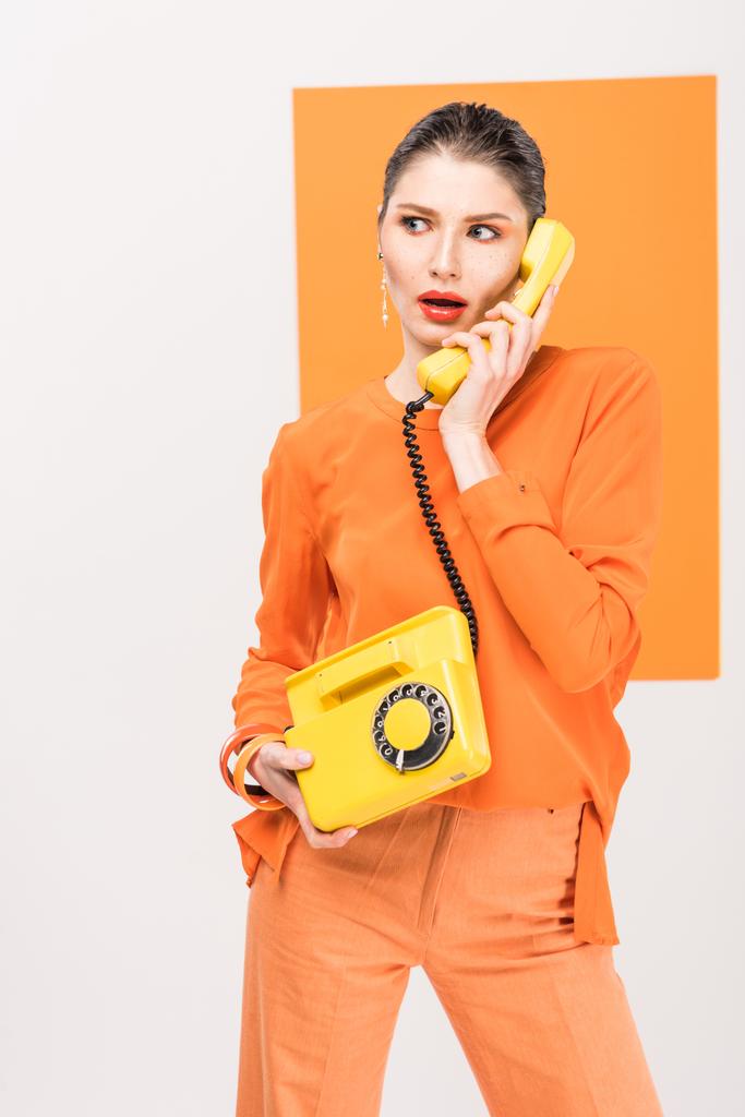 sorprendida mujer joven de moda hablando por teléfono retro y posando con cúrcuma en el fondo
 - Foto, Imagen