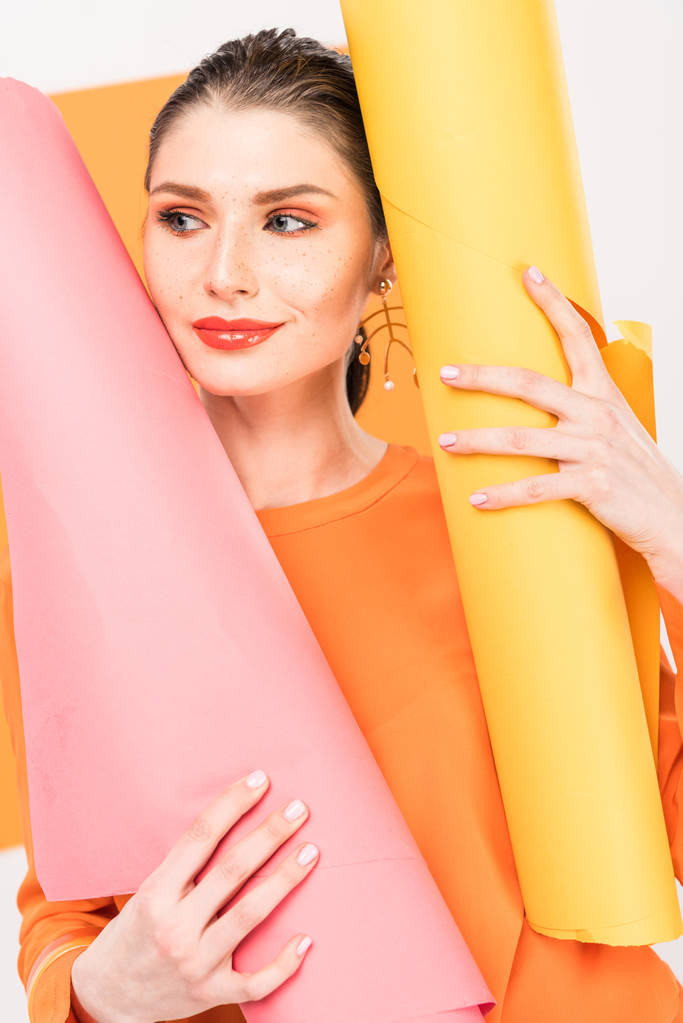 foco seletivo da jovem mulher elegante em roupas de açafrão sorrindo e posando enquanto segura rolos de papel
  - Foto, Imagem