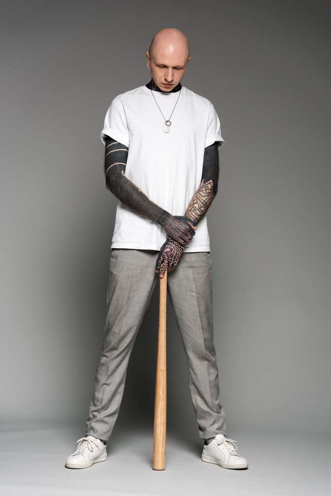 vue pleine longueur de l'homme tatoué chauve en t-shirt blanc tenant batte de baseball et regardant vers le bas sur gris
 - Photo, image