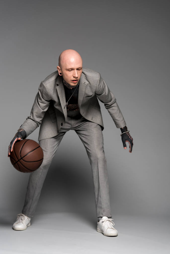 vista do comprimento total da elegante homem tatuado no terno jogando basquete na cinza  - Foto, Imagem