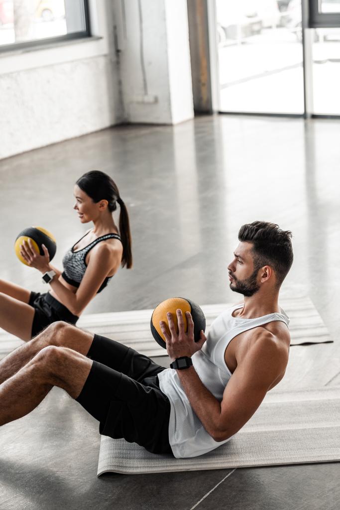 Blick aus der Vogelperspektive auf ein athletisches junges Paar, das Medizinbälle in der Hand hält und Bauchmuskelübungen auf Yogamatten macht - Foto, Bild