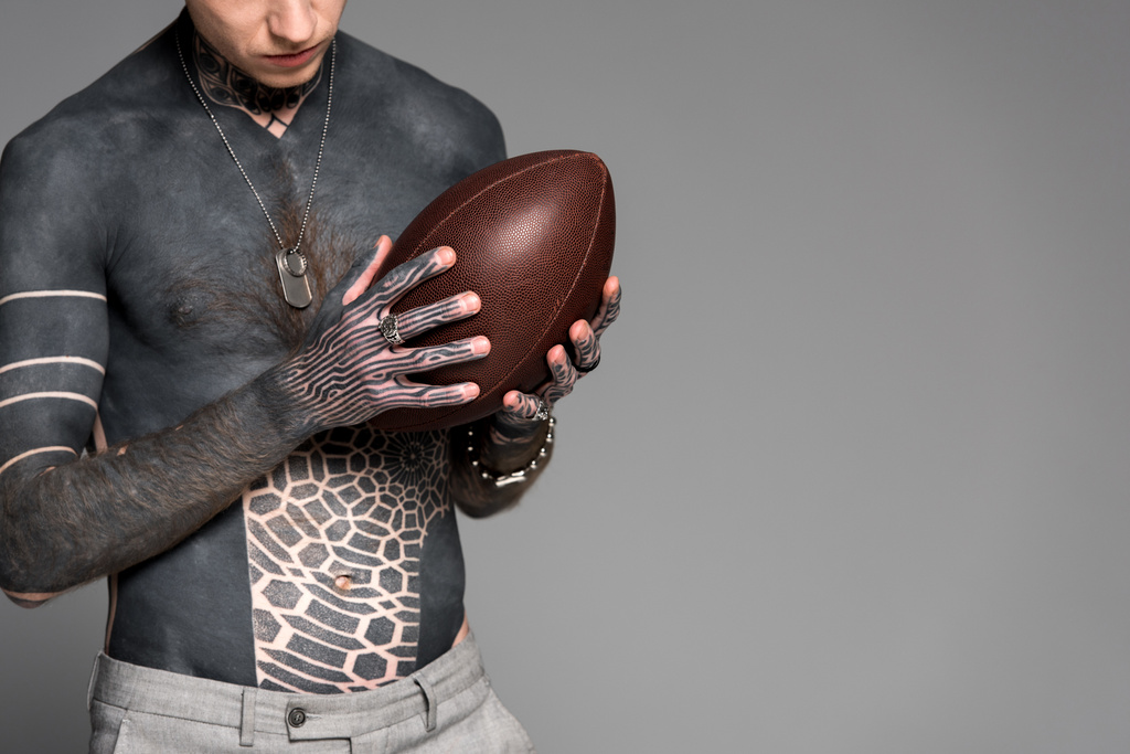 przycięte strzał człowieka gołe laski z tatuażami, trzymając rugby piłka na szarym tle - Zdjęcie, obraz