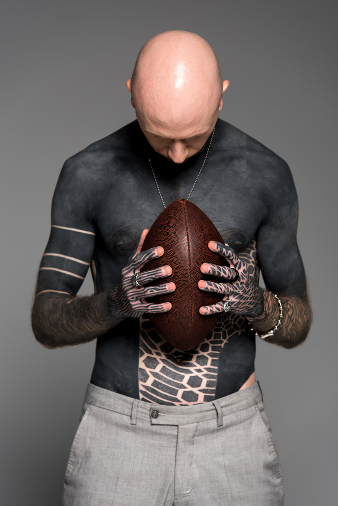 Glatzkopf tätowierter Mann hält Rugby-Ball isoliert auf grau - Foto, Bild
