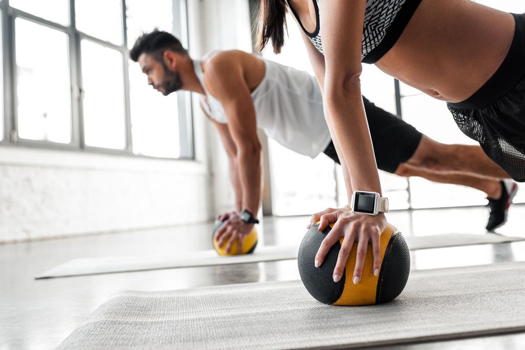tiro cortado de jovem casal esportivo exercitando com bolas de medicina em tapetes de ioga
 - Foto, Imagem