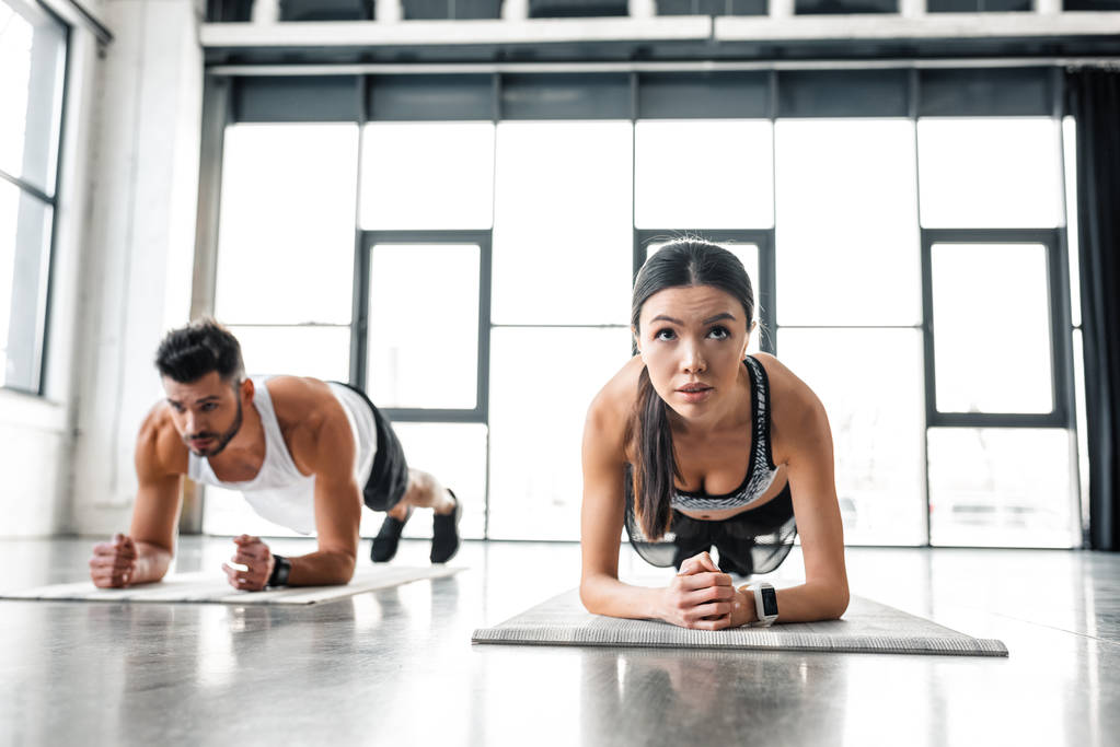 спортивний молодий чоловік і жінка в спортивному одязі роблять дошку вправи на килимках для йоги в спортзалі
  - Фото, зображення
