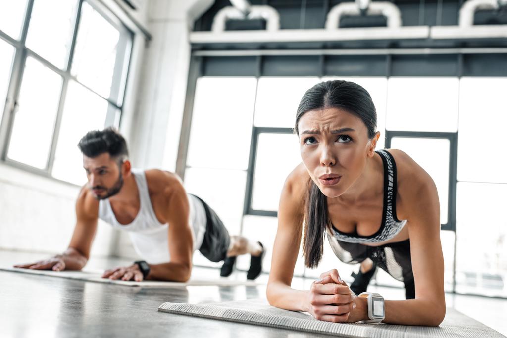koncentrovaný sportovní dívka a muž v tom prkně cvičení na jógu v tělocvičně sportovní oblečení  - Fotografie, Obrázek