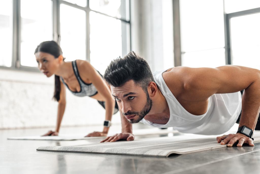 handsome young man and sporty girl doing push ups on yoga mats in gym - Photo, Image