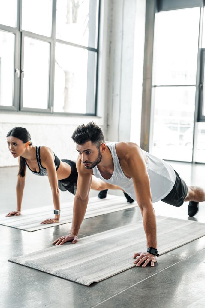 sportliches junges Paar in Sportbekleidung macht Liegestütze auf Yogamatten im Fitnessstudio  - Foto, Bild