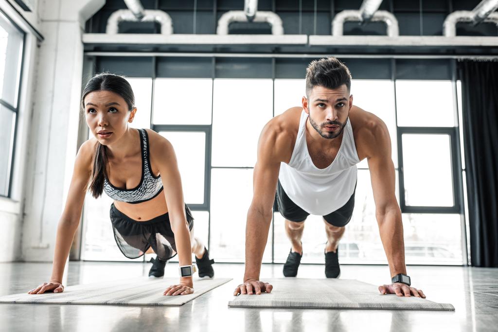 pareja joven y deportiva concentrada haciendo flexiones en colchonetas de yoga en el gimnasio
 - Foto, imagen