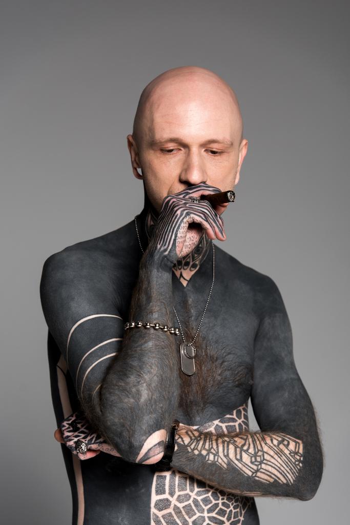 kopasz félmeztelen férfi tetoválás szivar dohányzás és lenézett elszigetelt szürke - Fotó, kép