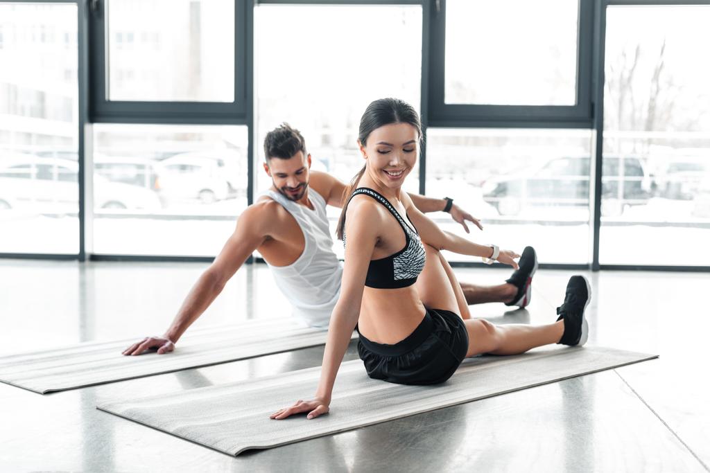 glückliches junges Paar sitzt auf Yogamatten und dehnt sich im Fitnessstudio - Foto, Bild
