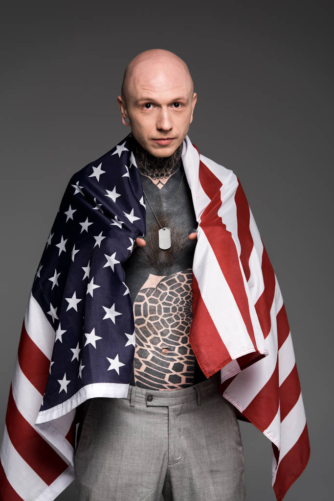 лысый мужчина без рубашки с татуировкой, стоящий рядом с нами флаг и смотрящий на камеру, изолированную на сером
 - Фото, изображение