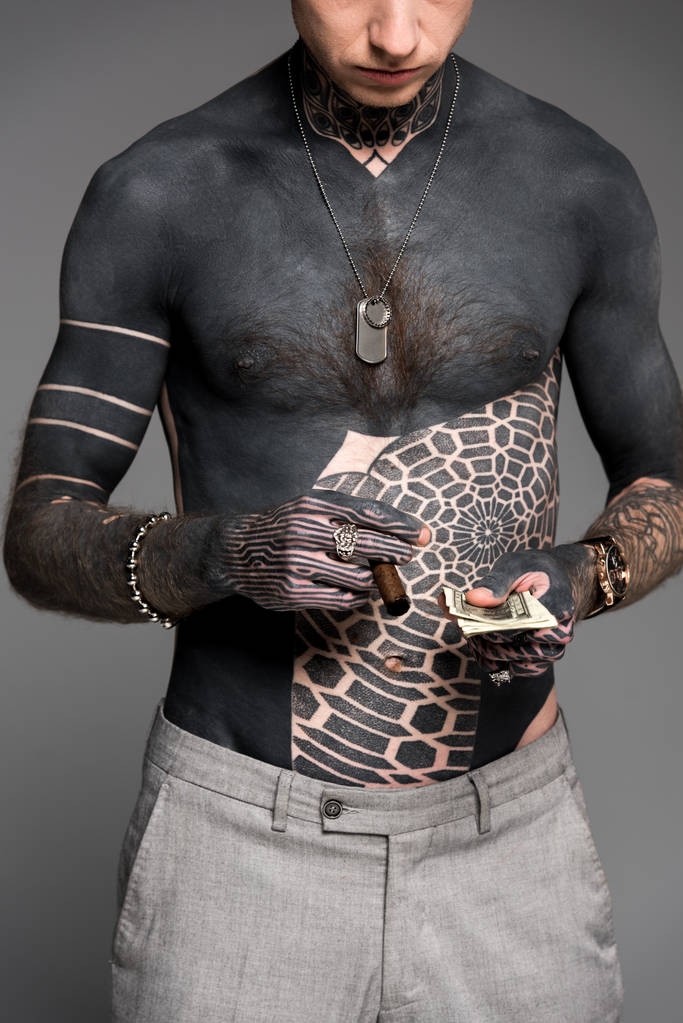 обрезанный снимок человека с татуировкой, держащего сигару и долларовые купюры, изолированные на сером
 - Фото, изображение