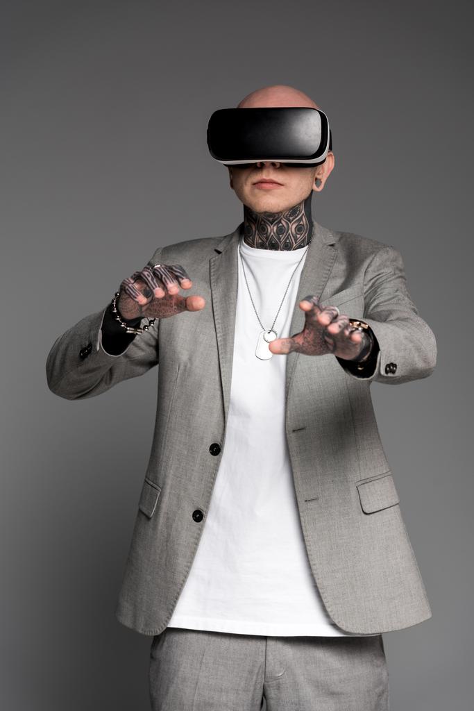kale getatoeëerd man in pak met behulp van virtual reality headset geïsoleerd op grijs   - Foto, afbeelding