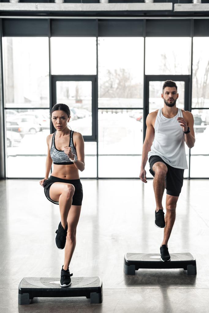 vista completa de la pareja joven atlética de entrenamiento en plataformas de paso en el gimnasio
  - Foto, imagen