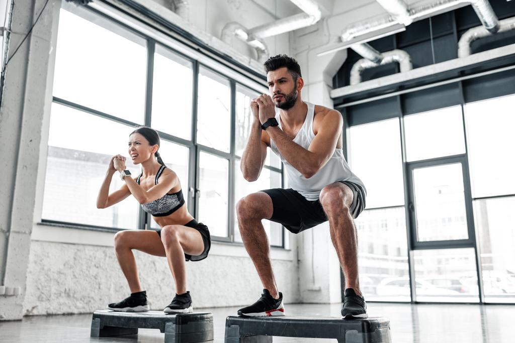 visão de baixo ângulo de casal jovem esportivo concentrado em treinamento de sportswear com plataformas passo no ginásio
  - Foto, Imagem