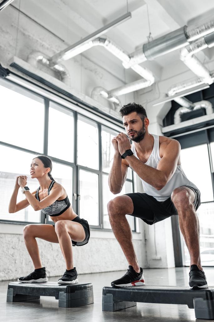 vue à faible angle du jeune couple athlétique dans l'entraînement de vêtements de sport avec des plates-formes pas à pas dans la salle de gym
  - Photo, image