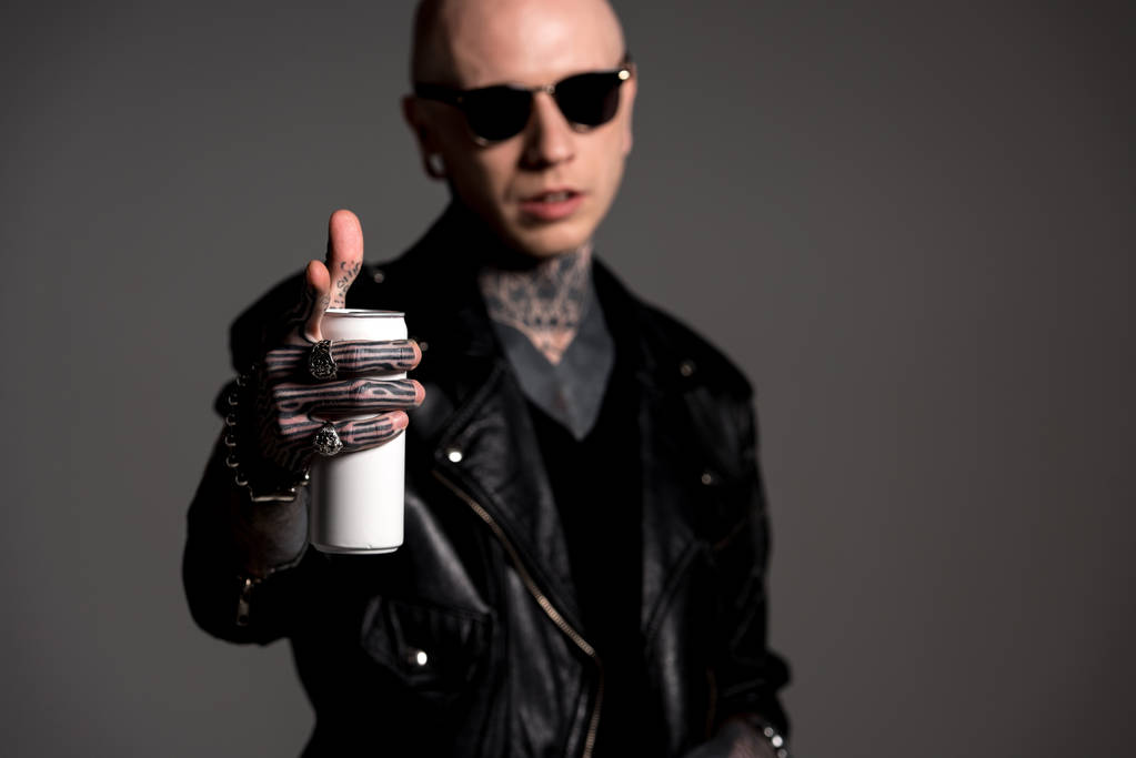 stylish tattooed man in leather jacket and sunglasses holding soda can and pointing at camera isolated on grey - Photo, Image