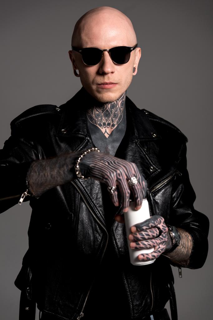 bald tattooed man in leather jacket and sunglasses opening soda can isolated on grey - Photo, Image