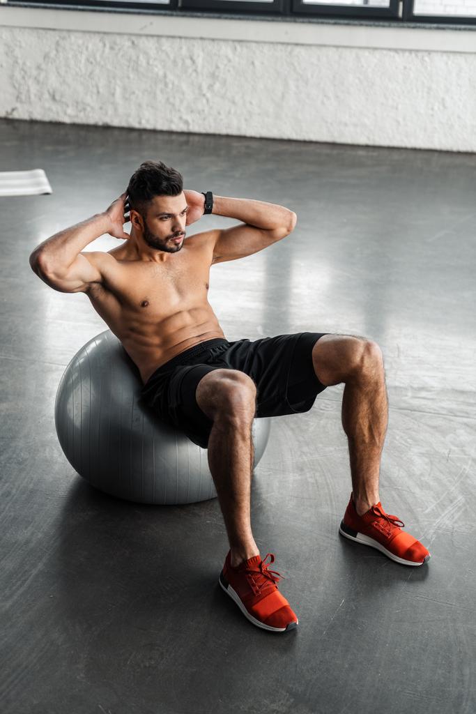 vue grand angle du jeune homme torse nu musclé faisant de l'exercice abdominal sur le ballon de fitness à la salle de gym
  - Photo, image
